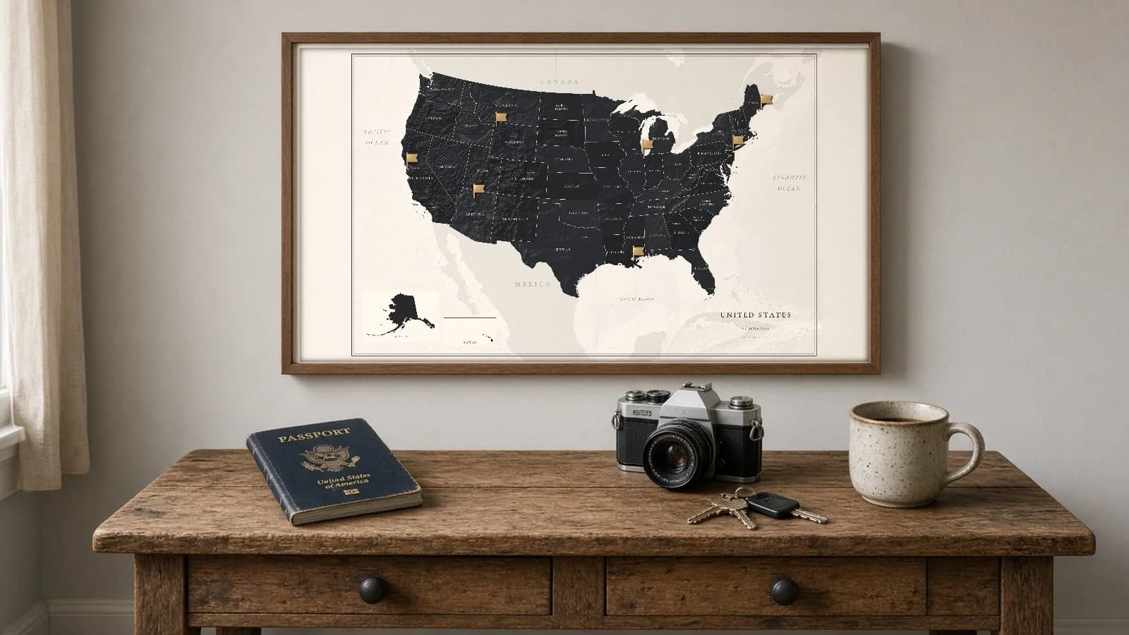 A dark framed United States map with gold pins above a desk holding a passport, camera, and keys.